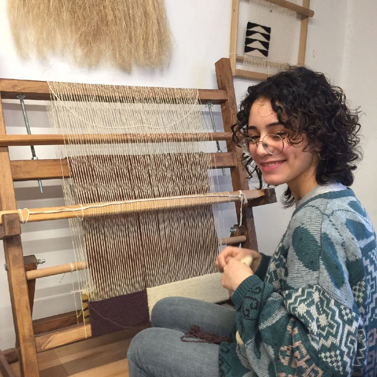 Product page bulletin second image, women crafter posing working on  a traditional rug loom